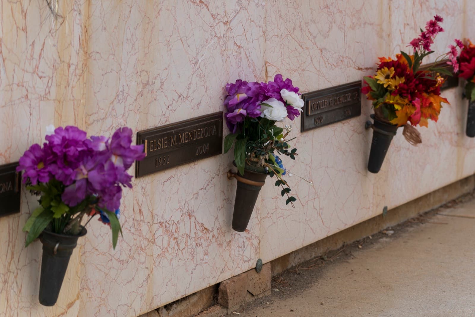 Colorful flowers in bronze vases along a memorial wall